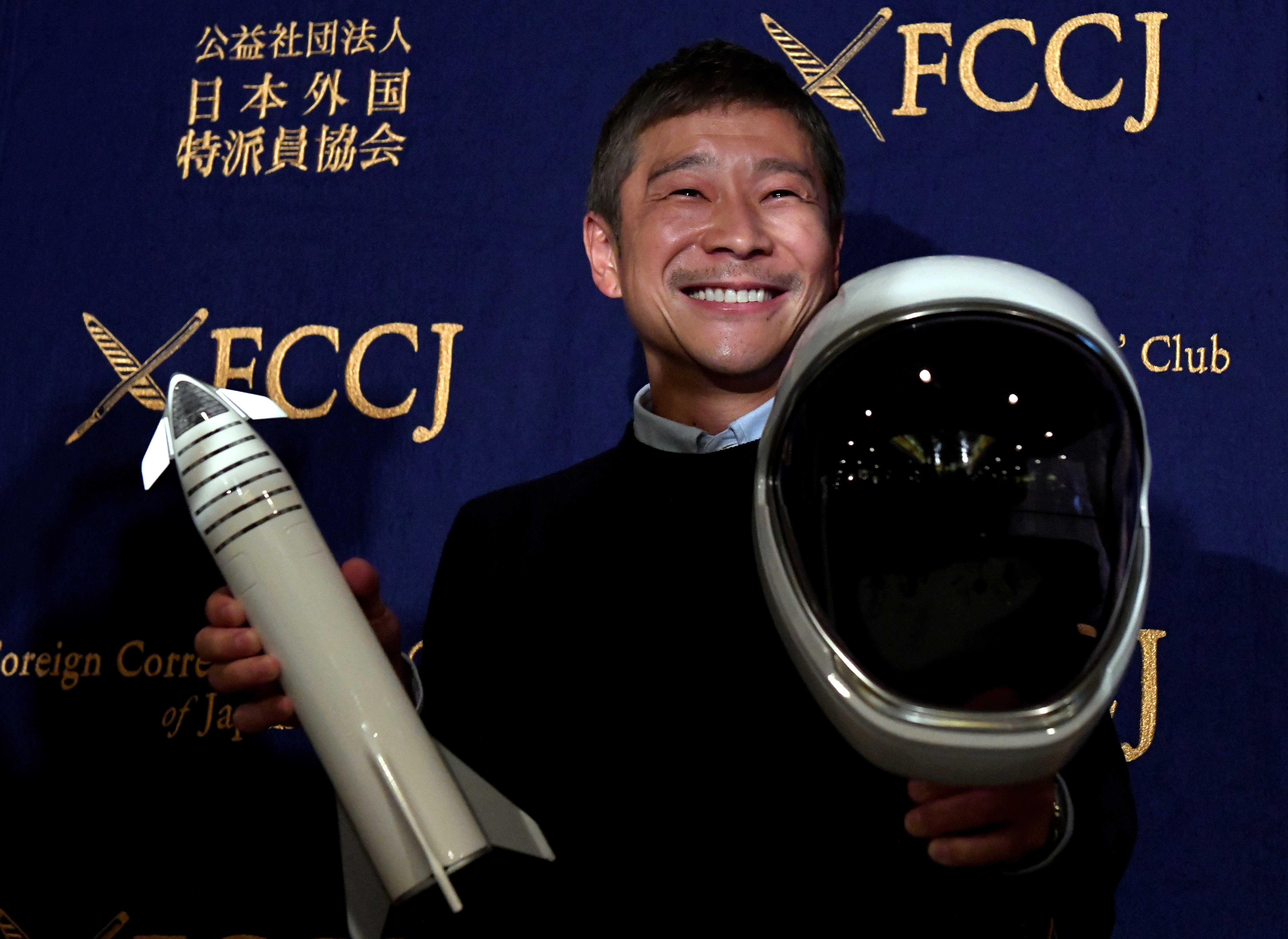 Yusaku Maezawa holding a model rocket and a space helmet.